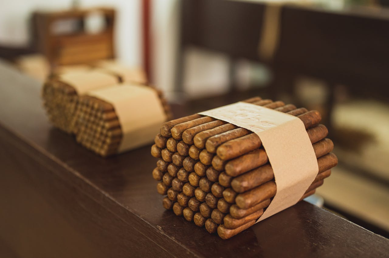 Stacks of cigar bundles wrapped in paper, placed on a wooden surface inside a manufacturing facility.